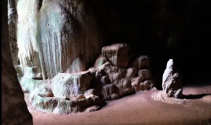 Inside Khao Pueng cave featuring striking geological formations — tiered mineral deposits resembling steps, vertical ridges of flowstone, and a stalagmite rising from the floor.