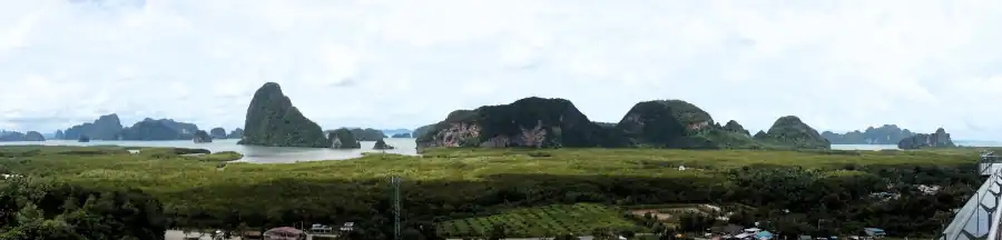 A sweeping view of dense forest leading to dramatic limestone karst formations, with waterways weaving through the terrain and small buildings visible at the edge of the greenery.