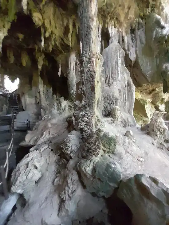A cave interior featuring stalactites, stalagmites, and a large column formation, with a constructed walkway and railings allowing visitors to explore safely.