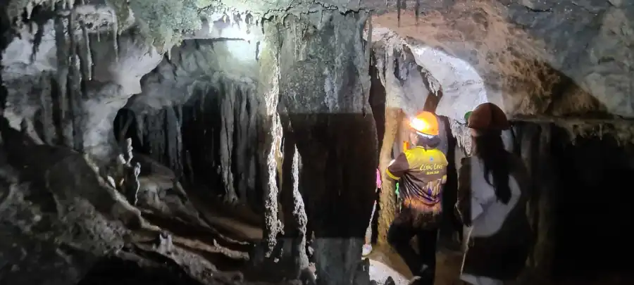 Visitors exploring a narrow limestone cave passage with stalactites and headlamps