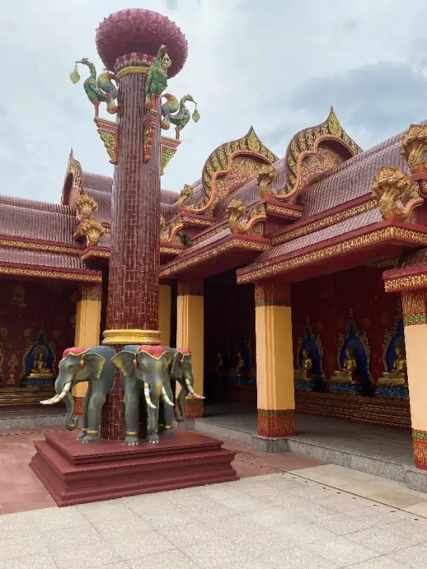 Intricate temple complex with tiered golden roofs, multiple spires, and surrounding gardens with tiled walkways beneath an overcast sky.