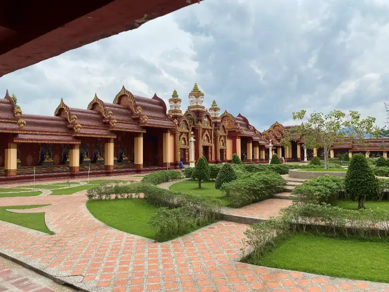 Decorated temple with red and gold roofing, column adorned with elephant sculptures, and golden Buddha statues inside alcoves.