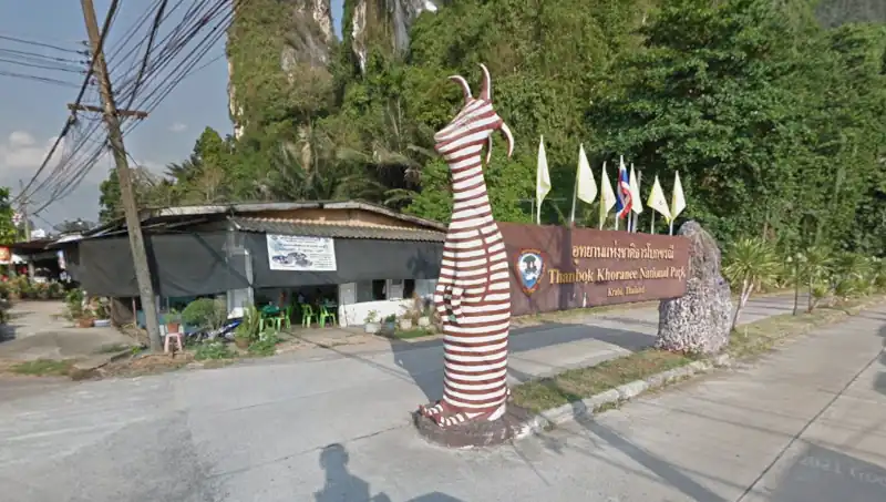 Than bok khorani National park entrance sign beside limestone cliffs and roadside buildings in tropical Thailand